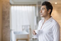 Hombre chino sosteniendo taza de café en casa - foto de stock