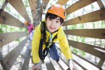 Chinese boy in tree top adventure park wooden tube — Stock Photo