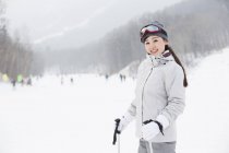 Chinese female skier standing with ski poles on slope — Stock Photo