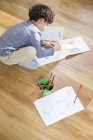 Азіатський елементарних вік хлопчик робить домашнє завдання на поверсі — стокове фото