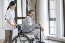 Chinese nursing assistant taking care of senior man in wheelchair — Stock Photo