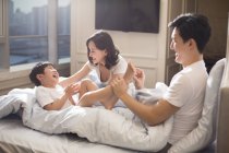 Chinese parents tickling son in bed — Stock Photo