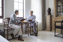 Hombres chinos mayores discutiendo mientras leen libros en la sala de estar - foto de stock