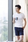Chinese hält Kaffee und schaut durch Fenster nach Hause — Stockfoto