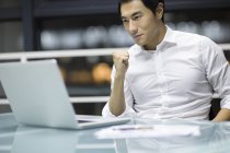 Empresário chinês torcendo na mesa com laptop no escritório — Fotografia de Stock
