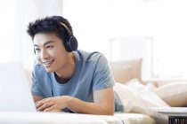Chinese man in headphones using laptop on sofa — Stock Photo