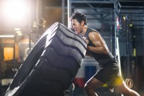Chino hombre empujando grande neumático en crossfit gimnasio - foto de stock