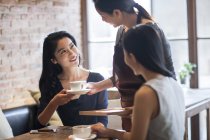 Chinese waitress serving coffee to female friends in cafe — Stock Photo