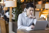 Chinese man using laptop in cafe — Stock Photo