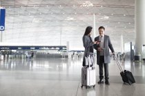 Asian man and woman looking at passports in airport lobby — Stock Photo