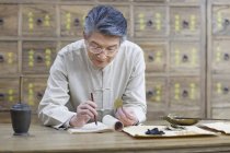 Mature chinese doctor examining medicinal herbs — Stock Photo