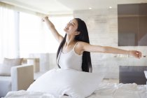 Chinese woman stretching in bed in morning — Stock Photo