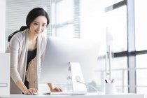 Усміхнена китайська жінка використовує комп'ютер в офісі — стокове фото