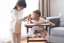 Little Chinese girl feeding baby boy in high chair — Stock Photo