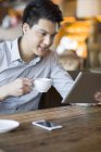Hombre chino usando tableta digital y taza de celebración en la cafetería - foto de stock