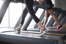 Vista recortada de pareja haciendo ejercicio en cintas de correr en el gimnasio - foto de stock