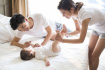 Chinese mother holding baby boy legs on bed with father — Stock Photo