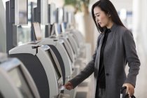 Азиатка пользуется билетным автоматом в аэропорту — стоковое фото