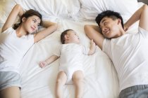 Famille chinoise avec bébé garçon couché sur le lit — Photo de stock