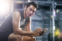 Chinese man using smartphone in gym — Stock Photo