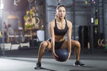 Chinese woman exercising with medicine ball at gym — Stock Photo