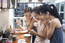 Amigos femeninos usando smartphone mientras beben café en la cocina - foto de stock