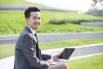 Empresário asiático usando laptop ao ar livre — Fotografia de Stock
