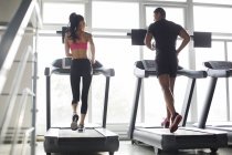 Pareja china haciendo ejercicio en cintas de correr en el gimnasio - foto de stock