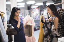 Amici cinesi di sesso femminile che scelgono tra i vestiti nel negozio di abbigliamento — Foto stock