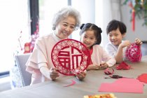 Внуки и бабушка с китайской новогодней вырезкой из бумаги — стоковое фото