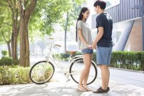 Pareja china cogida de la mano en el campus con bicicleta - foto de stock