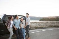 Chinese friends leaning on car in suburbs — Stock Photo