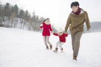 Familia china con hija corriendo sobre nieve - foto de stock