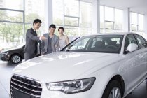 Chinese couple talking with dealer while choosing car in showroom — Stock Photo