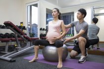 Pregnant woman working out with trainer at gym — Stock Photo