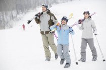 Genitori cinesi con figlio che cammina con gli sci sulle spalle nella stazione sciistica — Foto stock