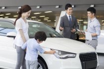Famille chinoise examinant la nouvelle voiture dans le showroom avec le vendeur de voiture — Photo de stock