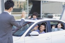 Chinesische Familie sitzt in Neuwagen und winkt Autoverkäufer zu — Stockfoto