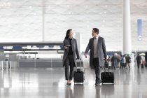 Chinese business people pulling wheeled luggage in airport lobby — Stock Photo