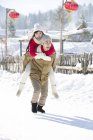 Chino hombre dando novia piggyback en snowy pueblo - foto de stock