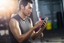 Chinese man using smartphone in gym — Stock Photo