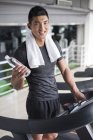 Chinese man holding bottle of water on treadmill — Stock Photo
