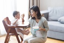 Китайская мать кормит мальчика в детском стульчике — стоковое фото