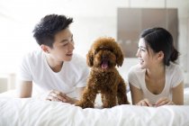 Chinese couple lying with pet poodle in bed — Stock Photo