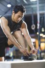 Азиатский спортсмен завязывает шнурки в спортзале — стоковое фото