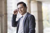 Портрет китайского бизнесмена, регулирующего очки в городе — стоковое фото