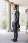 Chinese businessman with hands in pockets looking away in city — Stock Photo