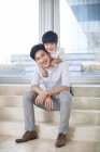 Menino chinês abraçando pai na sala de estar — Fotografia de Stock