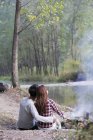 Chinese couple sitting on river bank in forest — Stock Photo