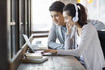 Chinese man and woman in headphones using laptop in cafe — Stock Photo